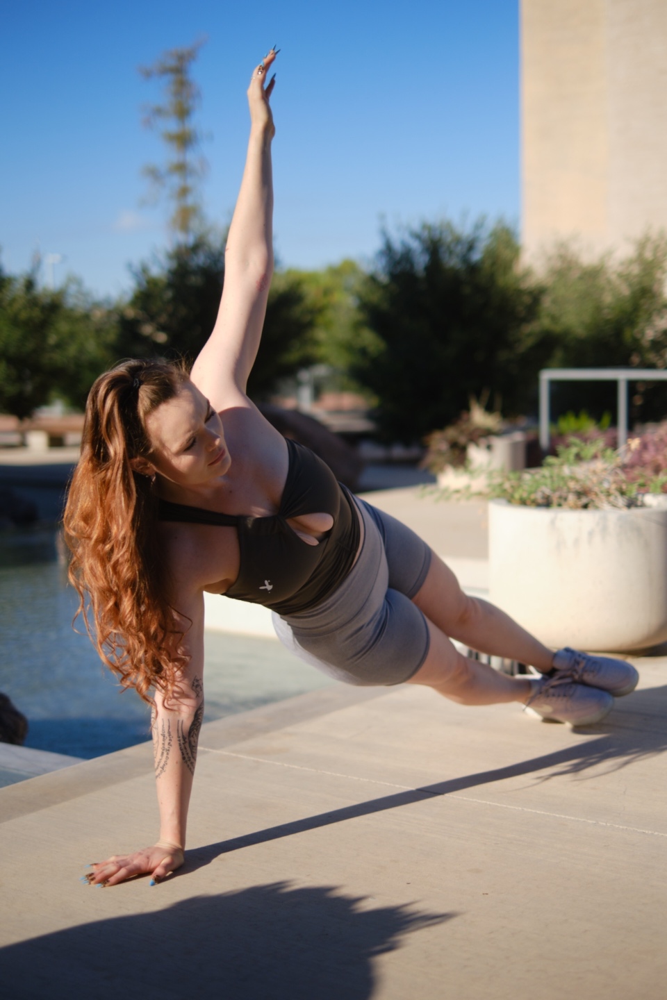 Coach Jamie doing a side plank outdoors by a pool, arm raised